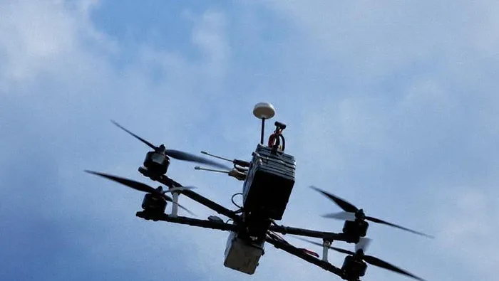 Quadcopter carrying an AURA onboard computer in flight against a blue sky